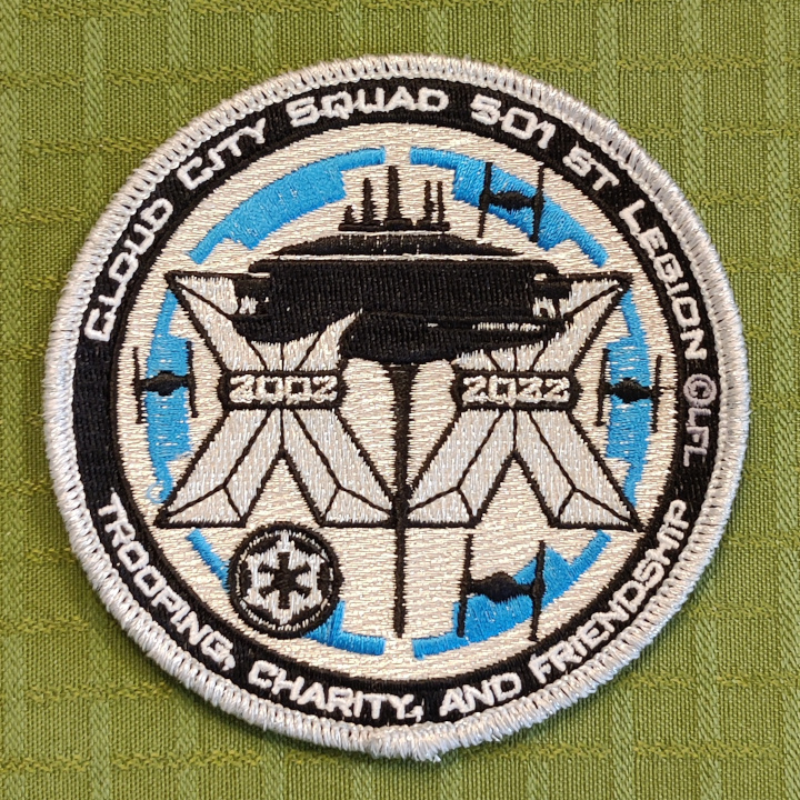 A black, blue and white embroidered patch. The patch is round.

The graphics is a cityscape view of Cloud City on Bespin in front of the roman numeral XX with the latin number 2002 on the left X and 2002 on the right X. There's four TIE fighers flying around. The background is the imperial cog. A smaller imperial cog is also seen. 
 
Along the frame it says "Trooping, charity, and friendship" and "Cloud City Squad 501st Legion".