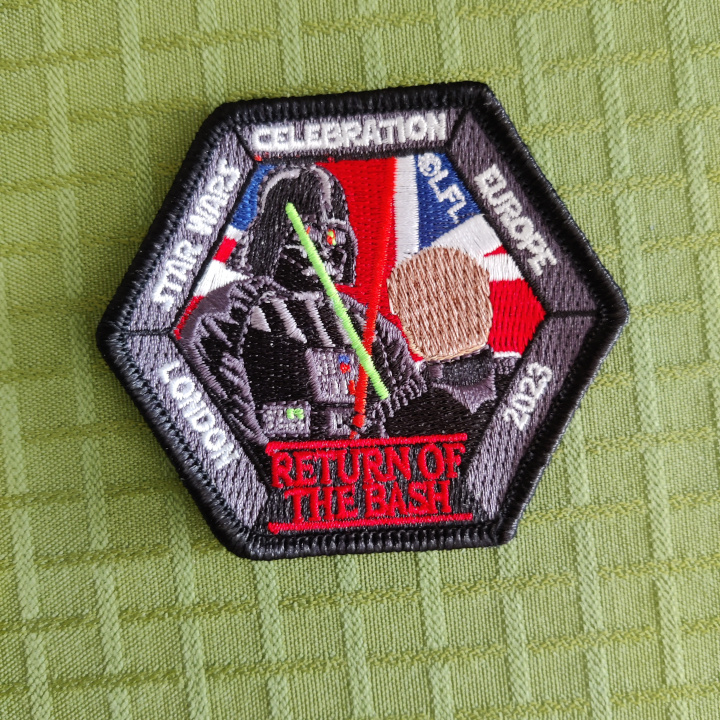 A hexagon shaped embroidered patch with Vader and Luke in a lightsaber duel in front of an Union Jack. The text around the border reads: "Star Wars Celebration Europe London 2023" and "Return of the Bash"