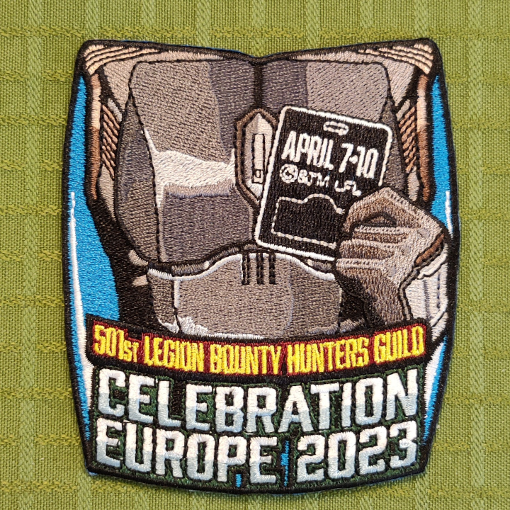 A rectangular, slightly oval, embroidered patch. A mandalorian armored wearing person is holding a badge. The badge reads "April 7-10". Text under the mando: "501st Legion Bounty Hunters Guild Celebration Europe 2023".