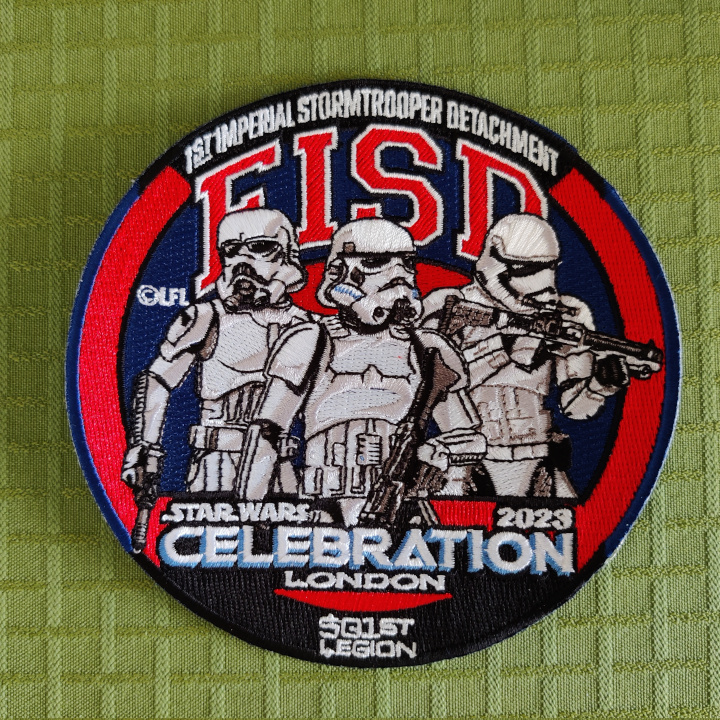 A round embroidered patch with three stormtroopers in front of a London Underground style sign. The text reads: "1st Imperial Stormtrooper detachment", "FISD", "501st Legion" and "Star Wars Celebration London 2023"
