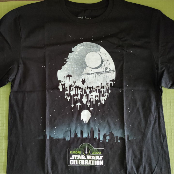 A black shirt. The graphic is the London cityscape at night. The second Death Star is looming above in the sky, but lots of rebel starships is coming to the rescue. Under the art is the Star Wars Celebration Europe 2023 logo.