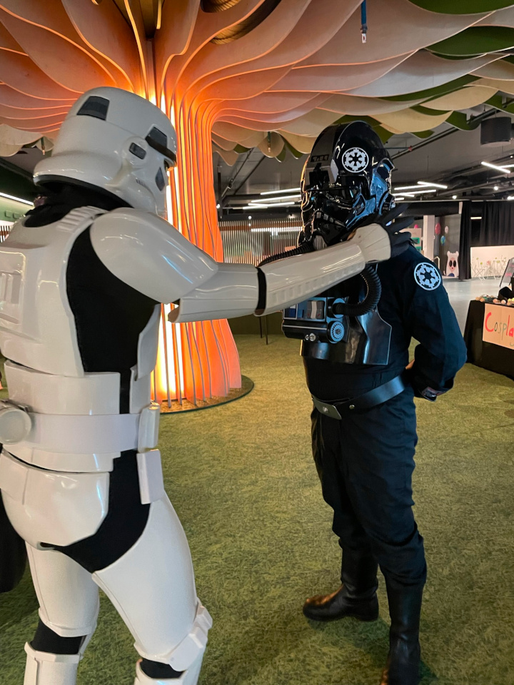A stormtrooper and a TIE pilot conversing under a tree-like installation.