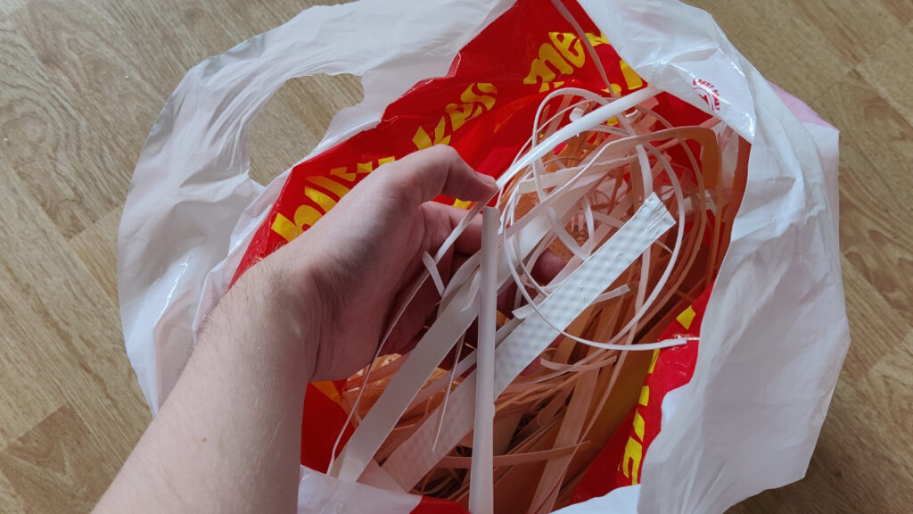 A grocery bag filled with white ABS plastic pieces in various shapes and sizes.