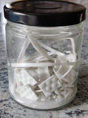 A glass jar filled with small pieces of white ABS plastic and acetone. The acetone is covering about 0,5 mm of the jar. The lid of the jar is on.