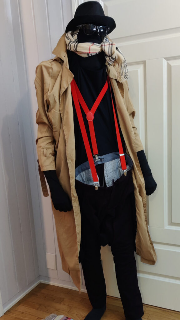 I am dressed as an invisible man. The costume is a beige coat with black lining, a pair of maroon pants with red suspenders, a hat, a scarf and a pair of sunglasses. The hat, glasses and scarf seems to be floating in thin air. The pants looks empty, but keeps the shape as though there's a body there.