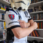 I am wearing the club shirt and my stormtrooper helmet. I am looking to the camera, holding my right arm towards it and pointing to the Norwegian Garrison logo on the sleeve.