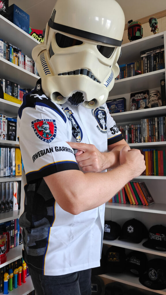 I am wearing the club shirt and my stormtrooper helmet. I am looking to the camera, holding my right arm towards it and pointing to the Norwegian Garrison logo on the sleeve.