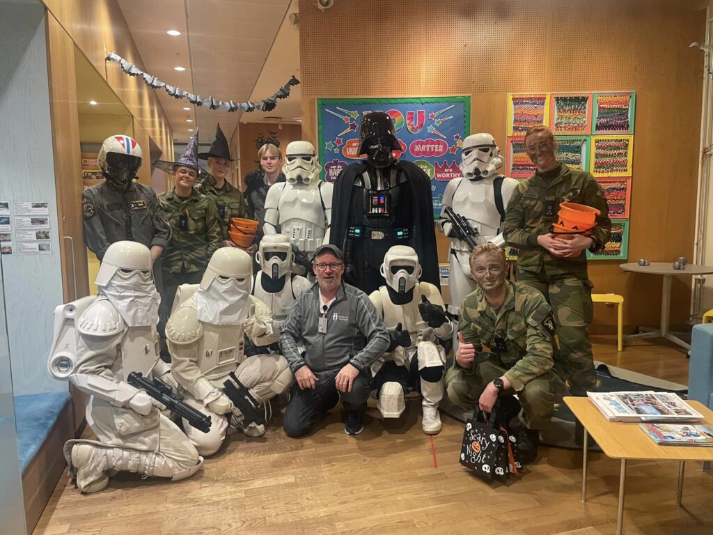 A group photo.
Top: A cadet in a grey flight suit and helmet, two cadets in green military uniform and witch hats, a cadet in grey flight suit and a fluffy toy spider on the shoulder, a stormtrooper (me), a Darth Vader, a stormtrooper, and a cadet in green military uniform and camouflage facepaint. Two of the cadets is carrying halloween buckets filled with candy to hand out.
Bottom: Two snowtroopers, a scout trooper, nurse Mads, a scout trooper, and a cadet in green military uniform and camouflage facepaint.