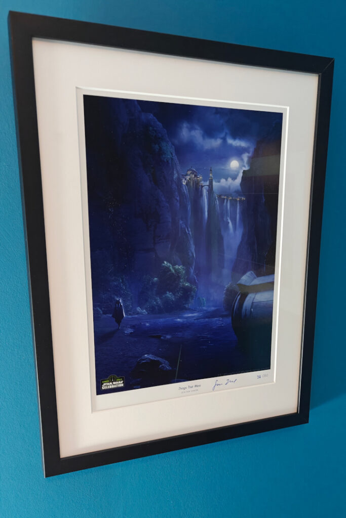 A framed artwork on a blue wall. We see a Naboo landscape at night with waterfalls in the distance. A hooded figure is visible in the moonlight. It's Ahsoka.