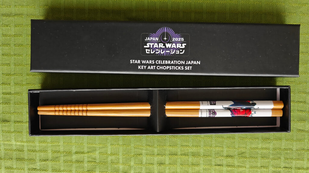 A black box with a chopstick set. The box features the Celebration 2025 logo. The chopsticks features the key art with Vader and Mt. Fuji.