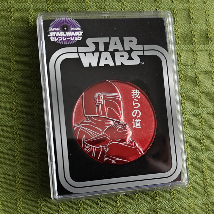A metal red challenge coin with The Mandalorian and Grogu.