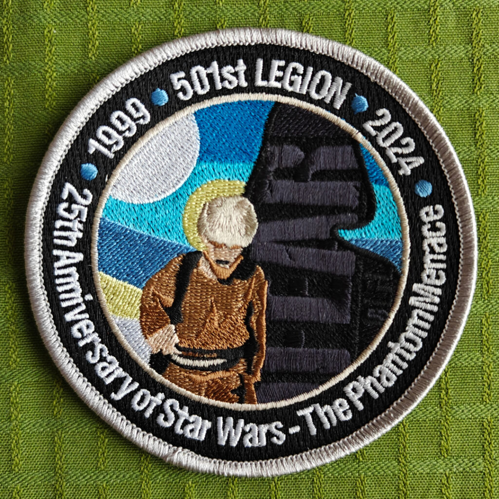 A round embroidered patch. We see Anakin Skywalker as a boy. His shadow looks like the shape of Darth Vader. Across the shadow is the word "FEAR". The border of the patch reads "1999. 501st Legion. 2014. 25th Anniversary of Star Wars - The Phantom Menace".