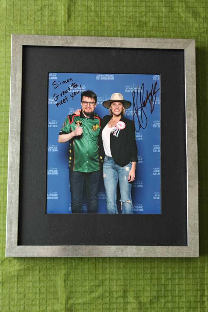 Me and Katee Sackhoff. I am wearing my club shirt, smiling nervously and giving a thumbs up to the camera. Sackhoff is wearing a large hat, a black jacket and a festive badge that says it's her birthday. She is smiling wide and holding an arm around my shoulders. The photo is signed; "Simon, great to meet you! Katee Sackhoff".